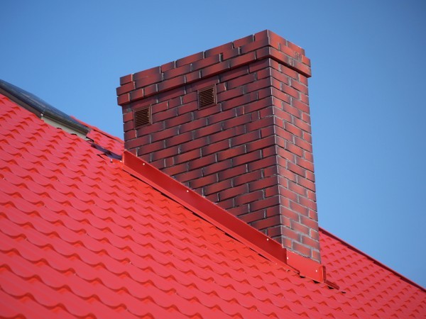 Wokół komina zakłada się w specjalnych bruzdach (10-15 cm powyżej pokrycia dachowego) wyprofilowane kołnierze blaszane. Fot. Shutterstock