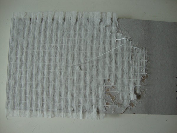 Próbka-tapety-przyklejonej-do-podłoża-po-badaniu-wytrzymałości-na-oddzieranie-(wydarciu-uległa-osnowa-tapety)